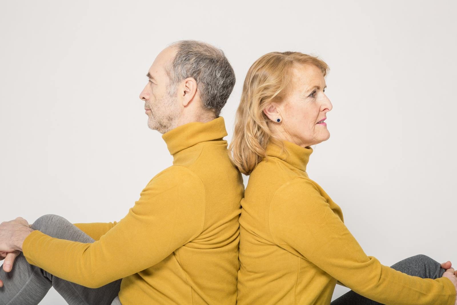 Elderly couple in yellow sweaters sitting back-to-back, symbolizing togetherness.