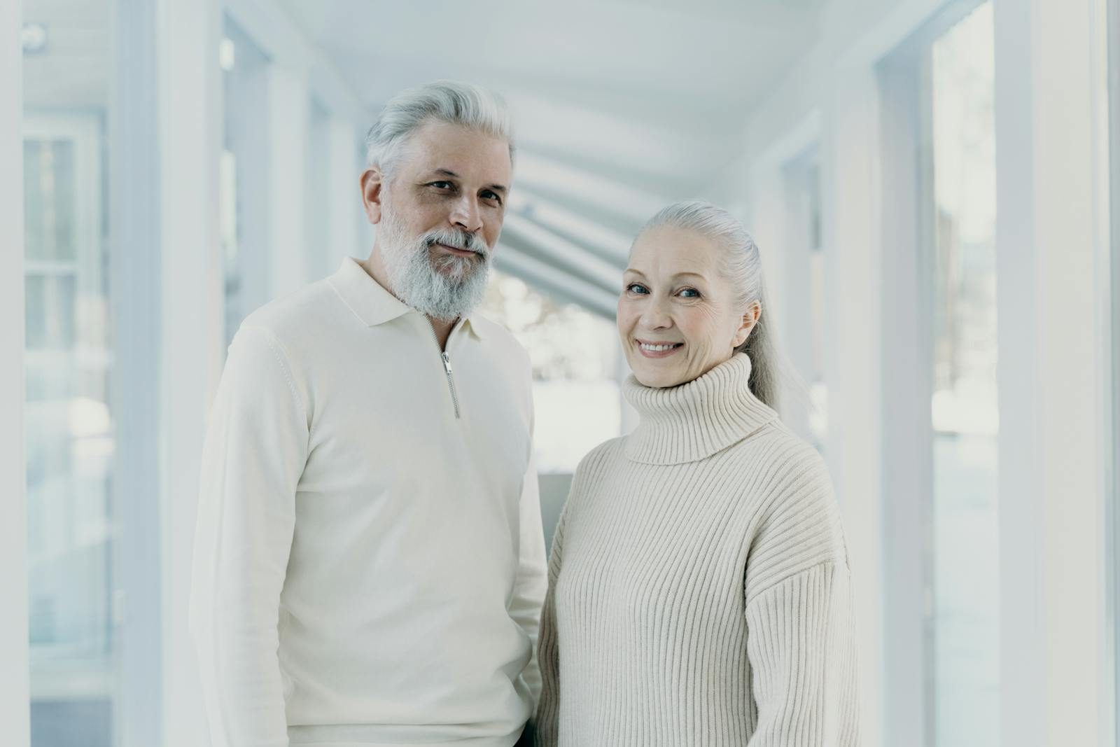 Happy senior couple wearing cozy sweaters, smiling inside a bright, modern space.