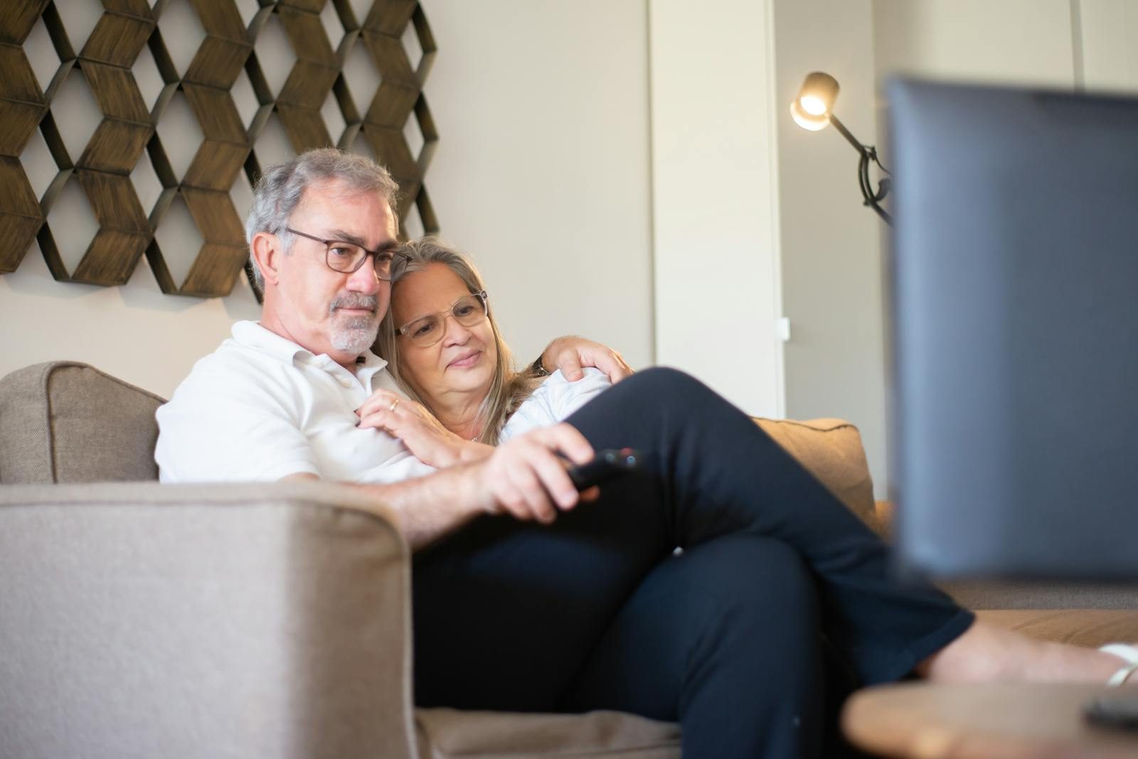 A senior couple enjoys a quiet and happy moment watching television together on the sofa.