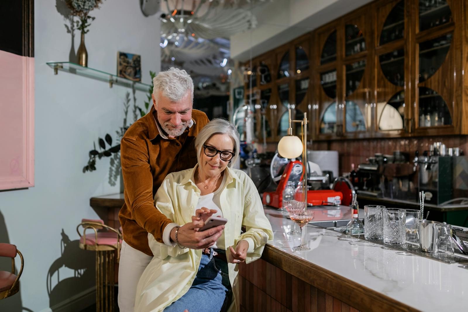 Elderly couple using a smartphone in a stylish cafe, showcasing togetherness and leisure.