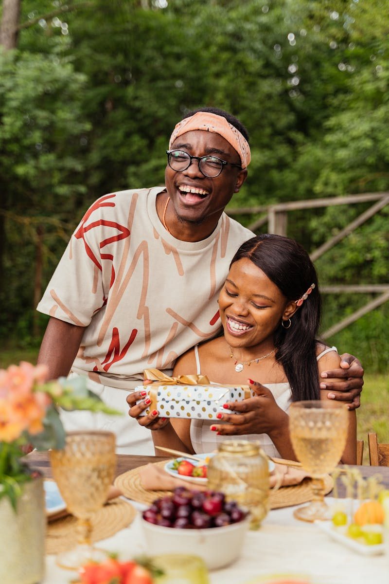 A cheerful couple exchanging gifts at a vibrant outdoor summer gathering, smiling and happy.