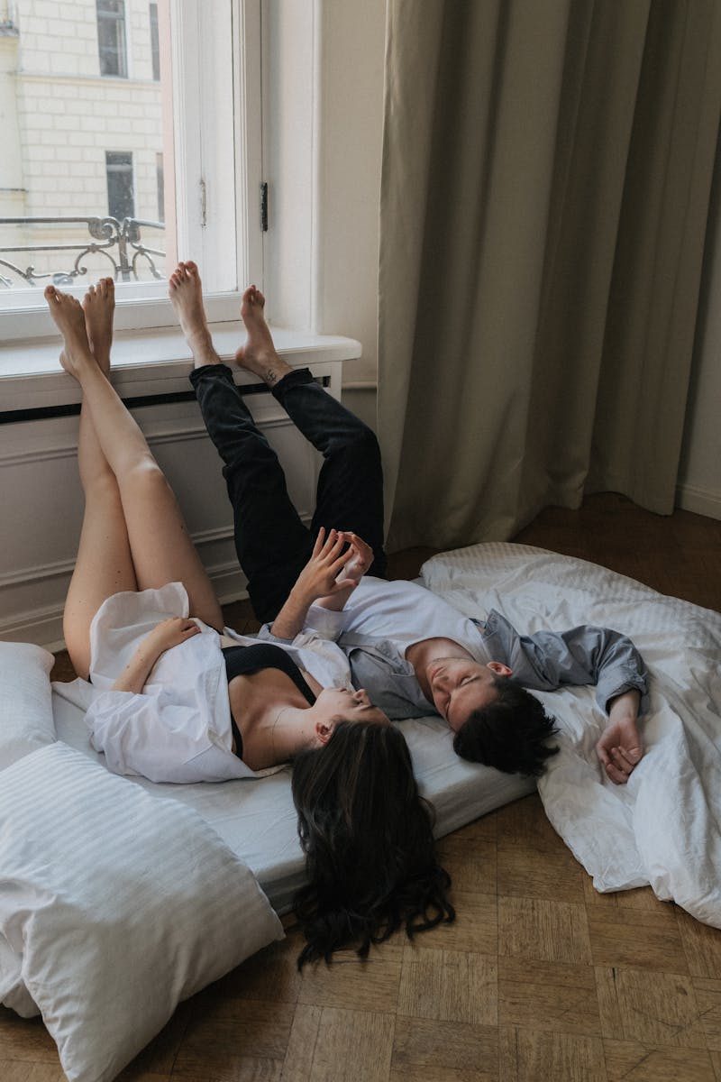 Couple lying on floor mattress near window, symbolizing love and relaxation.