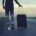 Man walking with a suitcase along a foggy road at sunrise, symbolizing adventure and travel.