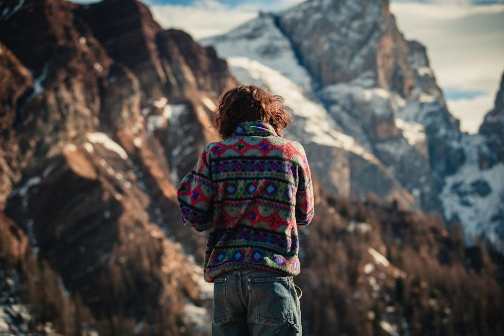 Back view of a woman in colorful sweater admiring the snowy mountains of Fiera di Primiero.
