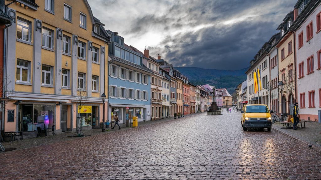 Picturesque European street scene with colorful buildings, cobblestones, and a yellow van.