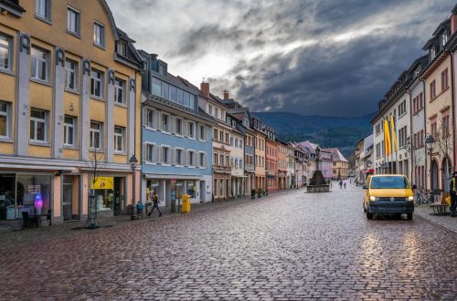 Picturesque European street scene with colorful buildings, cobblestones, and a yellow van.