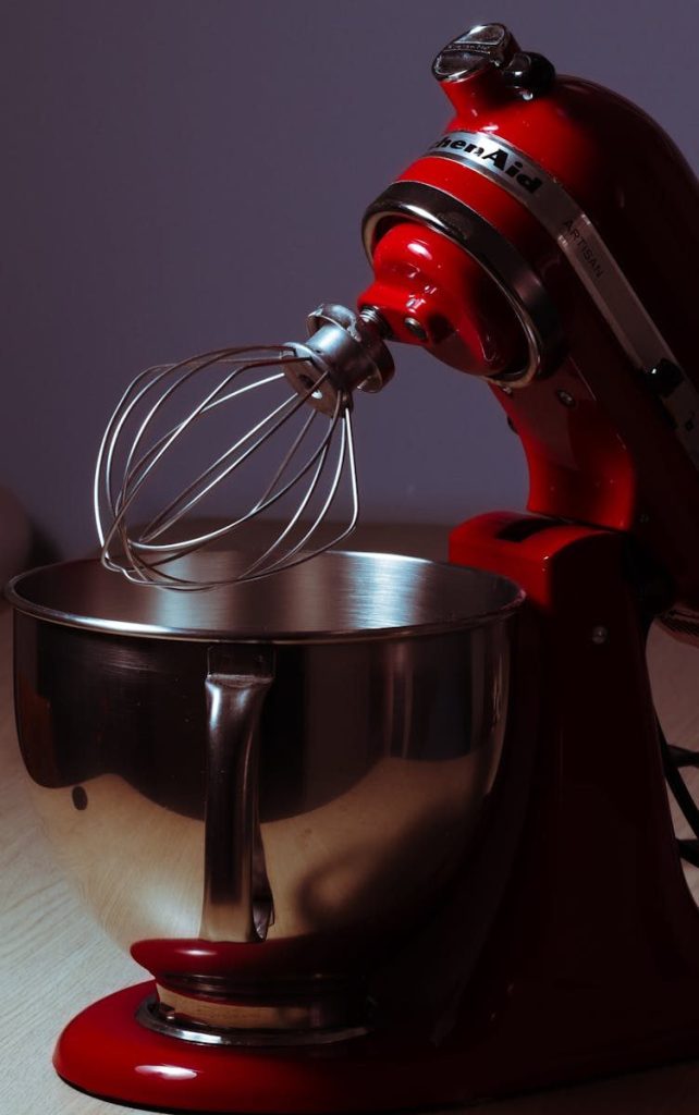 Red stand mixer with a chrome whisk and steel bowl on a kitchen countertop.