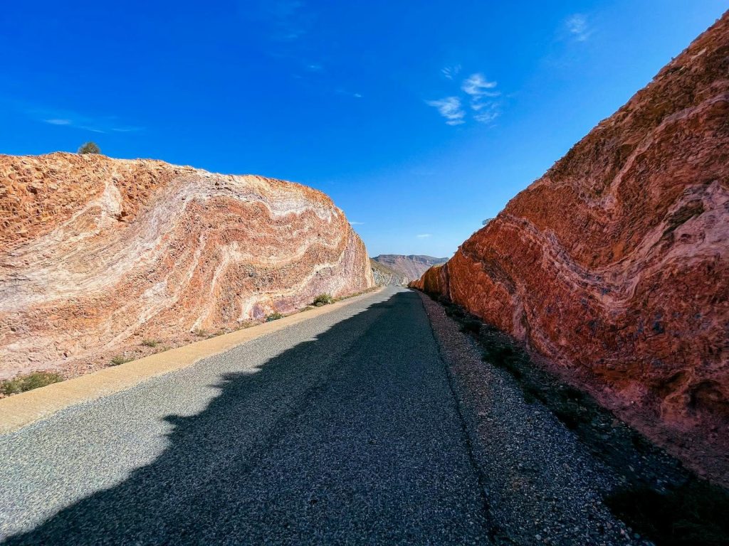 A scenic road winds through vibrant red cliffs in Tata, Morocco, under a clear blue sky.