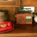 A vintage scene featuring a red rotary phone, old radio, and antique clock on a wooden shelf.