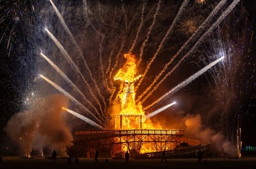 The iconic Burning Man effigy ablaze with surrounding fireworks at night.