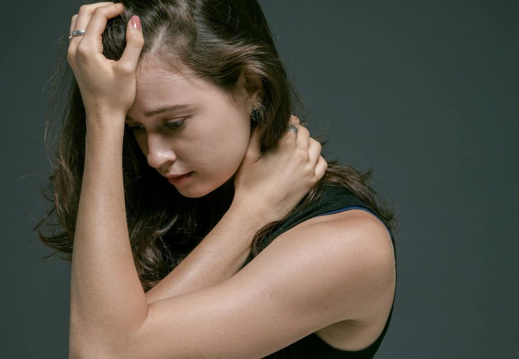 A woman in a sleeveless shirt appears pensive, holding her head with her hand. Deep contemplation is evident.