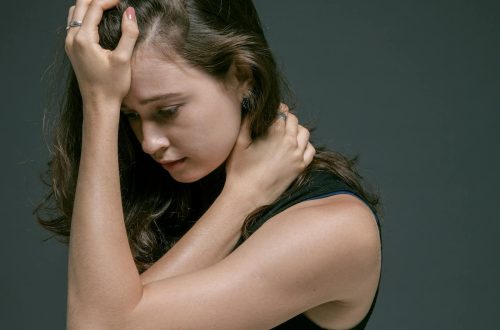 A woman in a sleeveless shirt appears pensive, holding her head with her hand. Deep contemplation is evident.