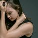 A woman in a sleeveless shirt appears pensive, holding her head with her hand. Deep contemplation is evident.