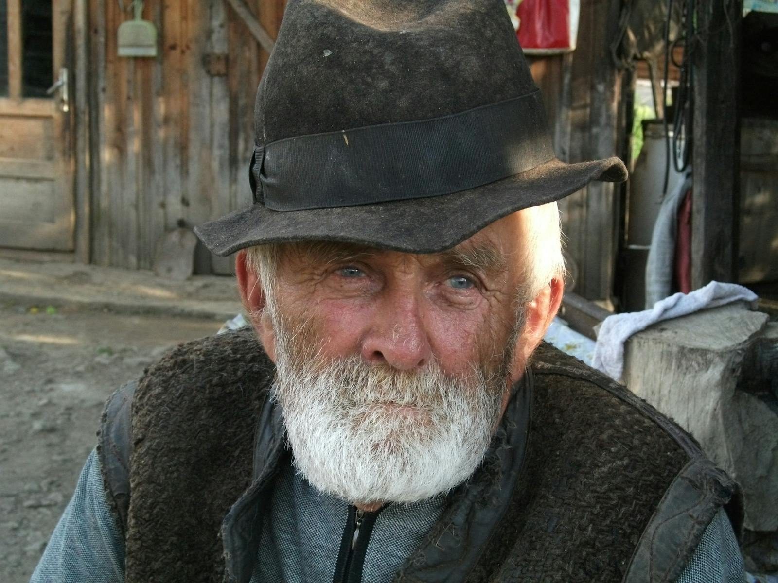 Close-up portrait of an elderly farmer with a beard and hat, with rustic wooden background.