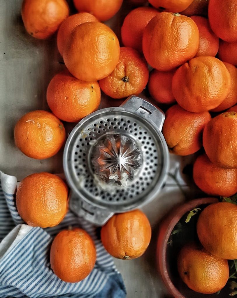 A collection of fresh oranges surrounding a metallic citrus juicer, viewed from above.