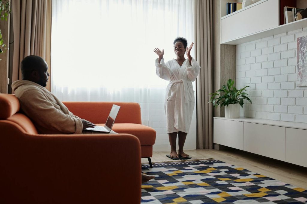 Couple relaxing at home, man using laptop and woman in bathrobe, in a bright modern living room.