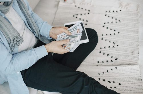 Close-up of adult counting cash with a tablet indoors, symbolizing finance and technology.