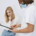 A doctor in a face mask discusses diagnosis with a patient in a clinic setting.