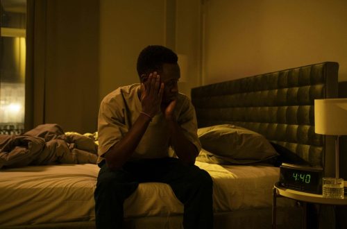 African American man sitting on a bed struggling with insomnia at night.