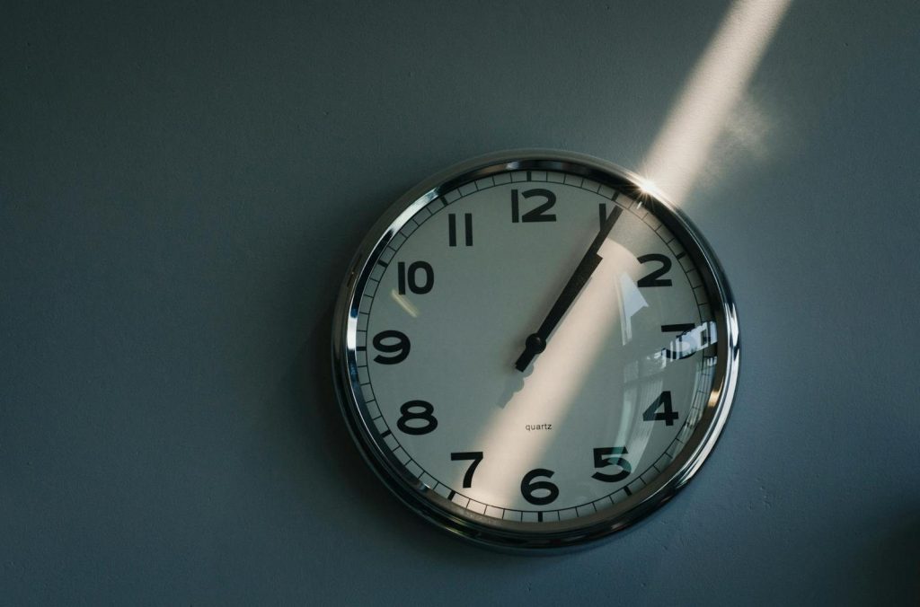 Close-up of a round wall clock illuminated by sunlight indoors, reflecting time passage.