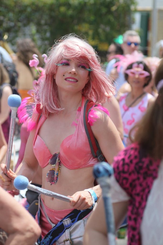 A joyful parade performer in vibrant pink attire with matching hair entertains during a lively festival.