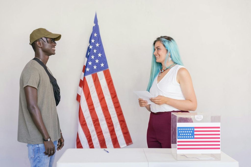Two diverse young adults engaging in a voting process next to an American flag.