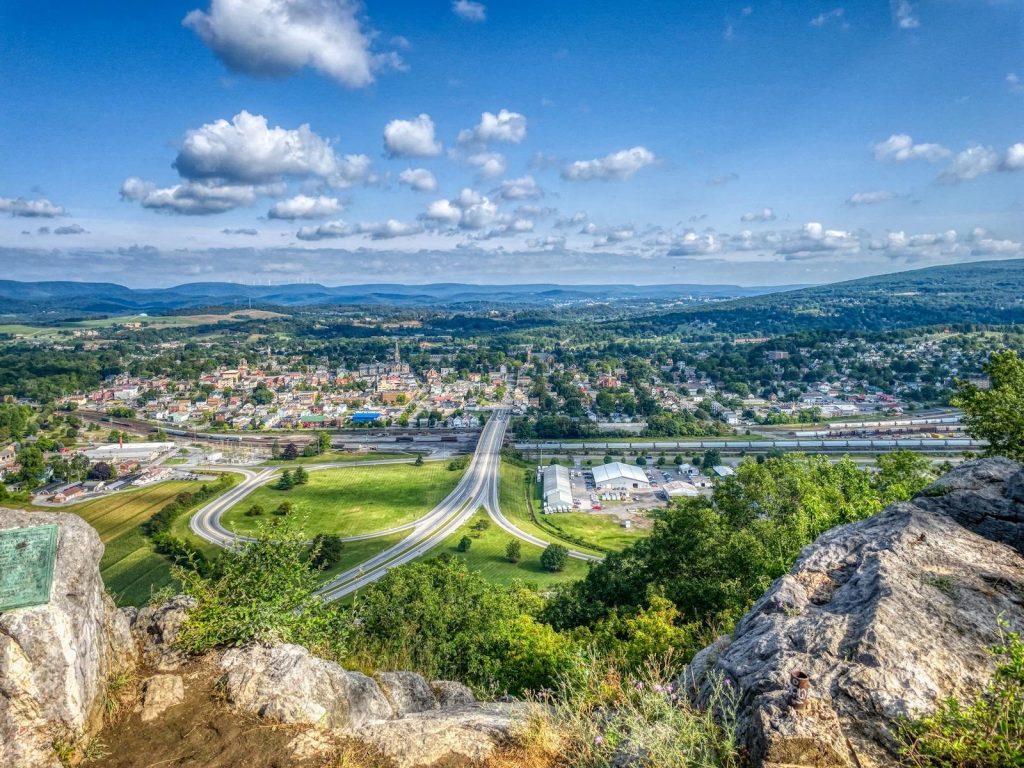 A breathtaking aerial view of Hollidaysburg, PA with rolling hills, roads, and clear blue sky.