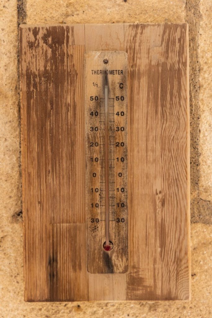 A close-up of an aged wooden thermometer mounted on a brick wall showing temperature in Celsius.