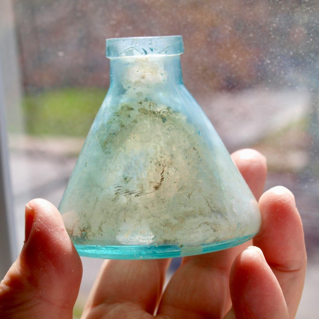 a hand holding a small glass vase with dirt inside of it